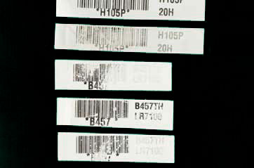 Close up of several barcode labels with varying degrees degradation obscuring their text.