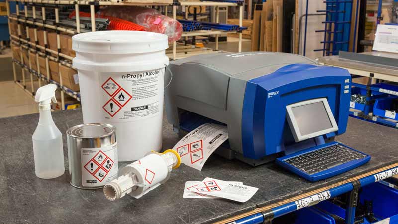 A Brady BBP85 THT benchtop printer sitting on a warehouse bench printing out GHS labels to communicate warnings to workers.
