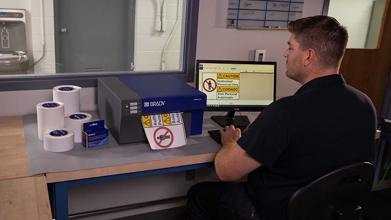 Worker printing out a bilingual "caution authorized personnel only" sign on a Brady J4000 Inkjet benchtop printer.