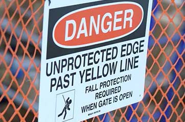  A sign on a construction fence. It says 'DANGER, UNPROTECTED EDGE PAST YELLOW LINE.'