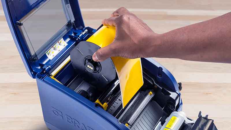 A roll of yellow label tape being loaded into a benchtop printer.